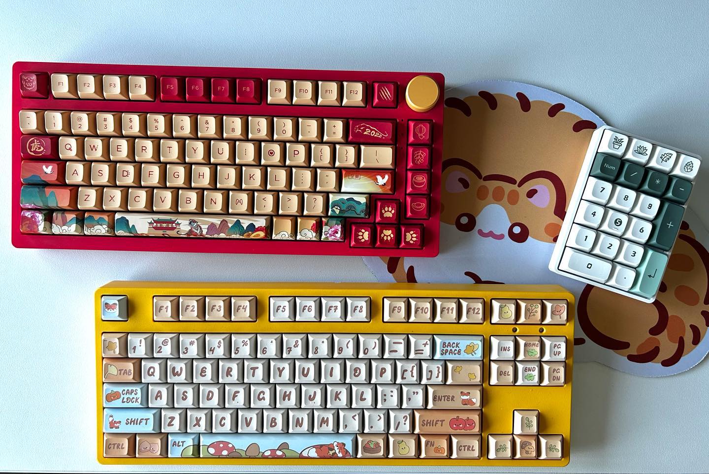 Two colorful custom mechanical keyboards and a matching numpad on a desk mat